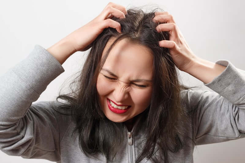 Vrouw heeft last van jeuk aan haar hoofd en krabt met haar handen op haar hoofd.